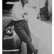 A black and white image of a young Malagasy man leaning against a car